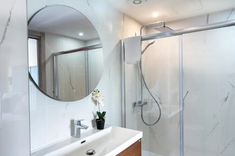 Une salle de bain moderne avec douche à l'italienne et grand miroir rond.