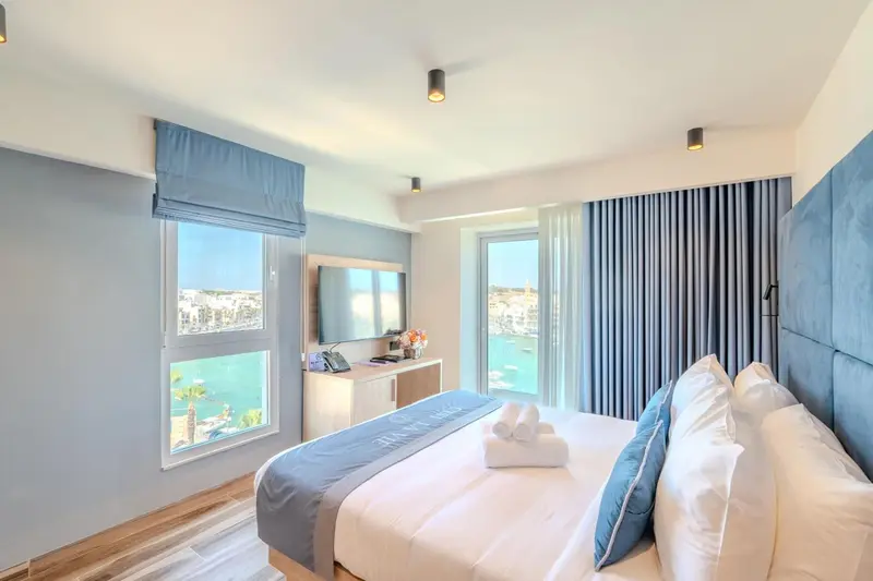 Chambre lumineuse avec un lit fait et une vue sur la mer par la fenêtre.