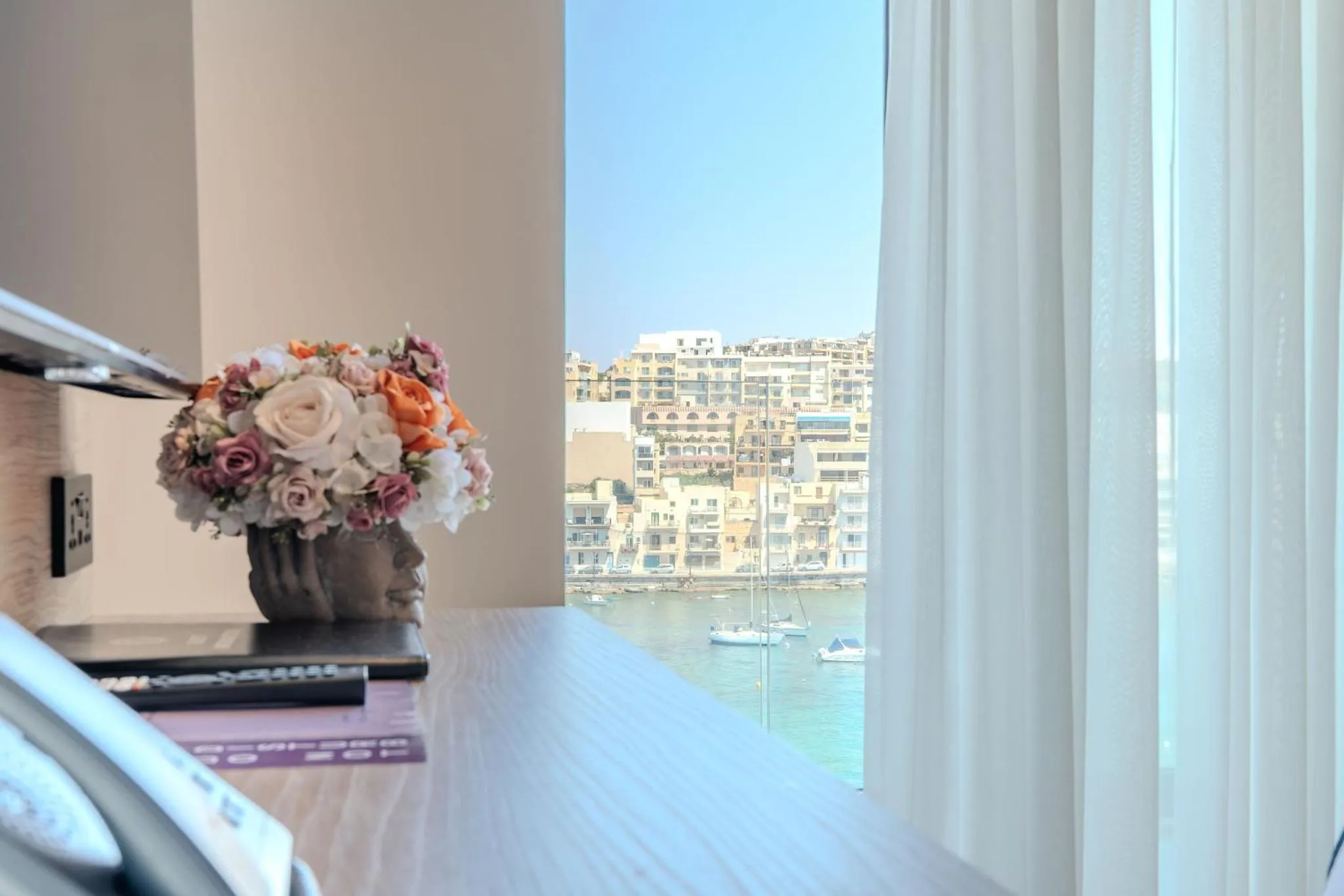 Un bouquet de fleurs orne une console avec vue sur la mer et des bateaux.