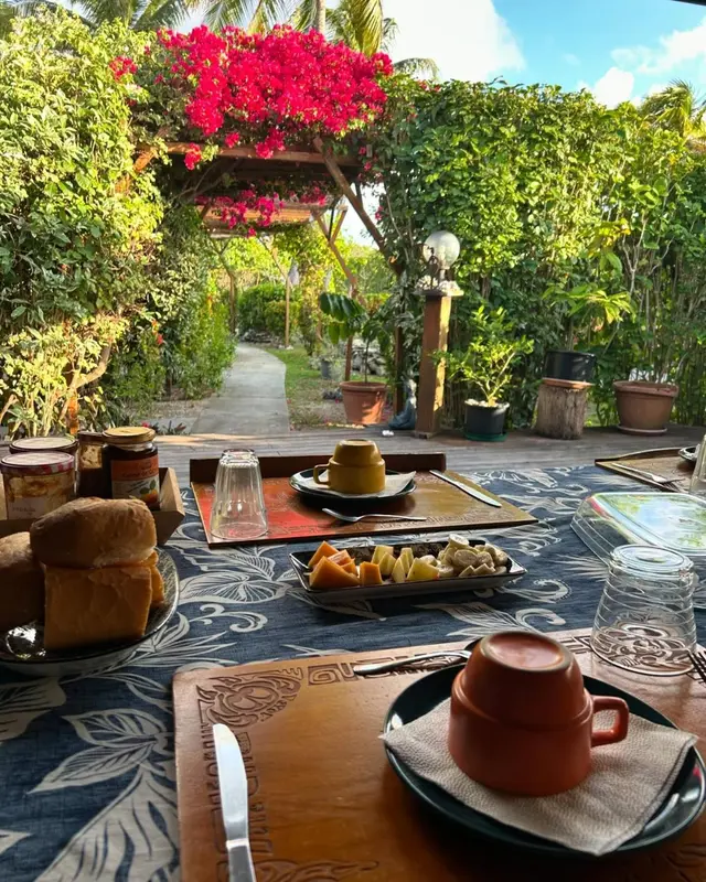 Une table est dressée avec un petit-déjeuner en extérieur, dans un jardin luxuriant.