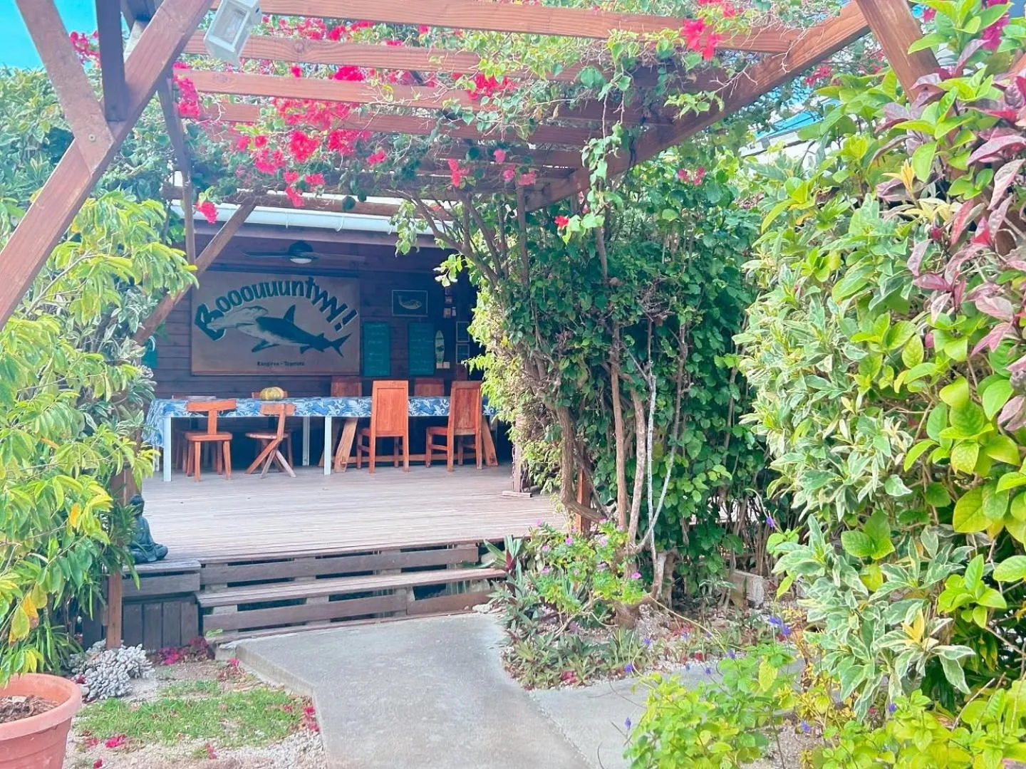 Terrasse en bois ombragée avec tables et chaises devant un bâtiment.