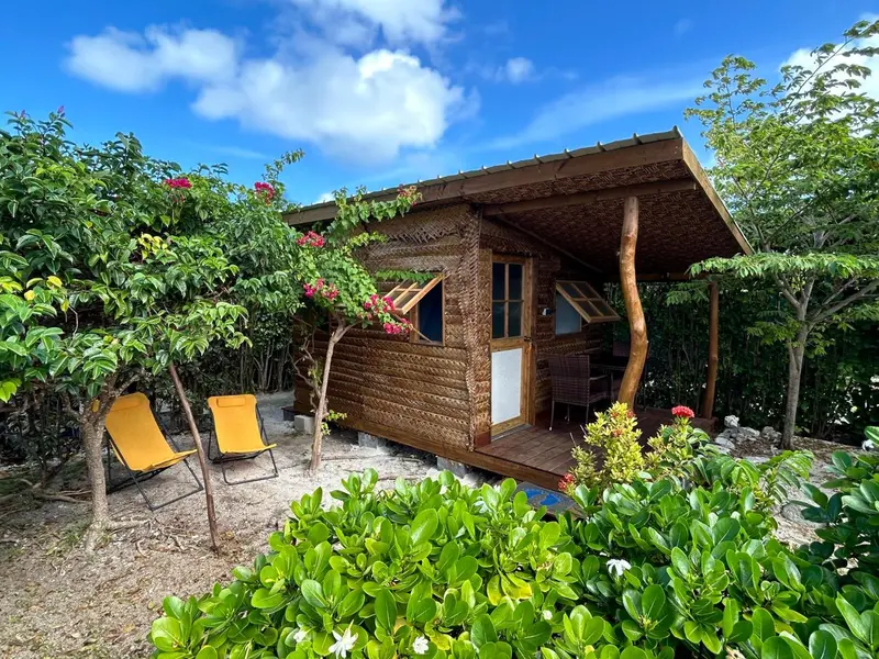 Petite cabane en bois et en paille avec deux chaises longues devant.