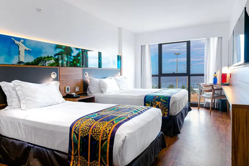 Une chambre lumineuse avec deux lits et vue sur la mer.