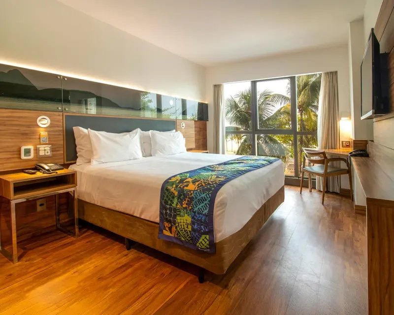 Une chambre lumineuse avec un grand lit et une vue sur la végétation.