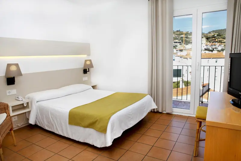 Une chambre lumineuse avec un lit recouvert d'une couverture verte et une vue sur la ville.