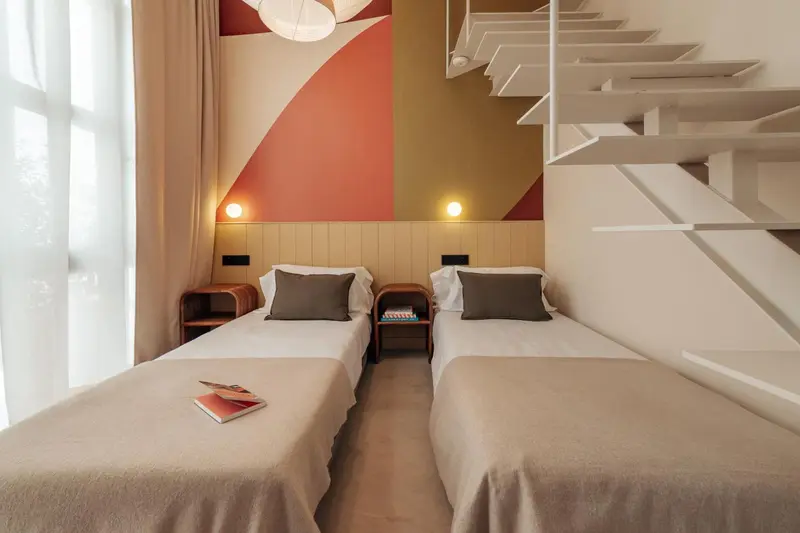Chambre avec deux lits simples et décoration murale géométrique.