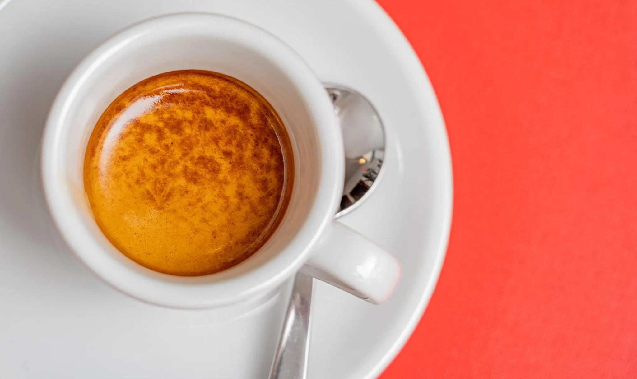 Une tasse de café espresso sur une soucoupe blanche, accompagnée d'une cuillère.