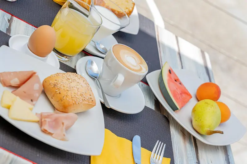 Une table est dressée pour un petit-déjeuner avec des viennoiseries, des fruits et des boissons.
