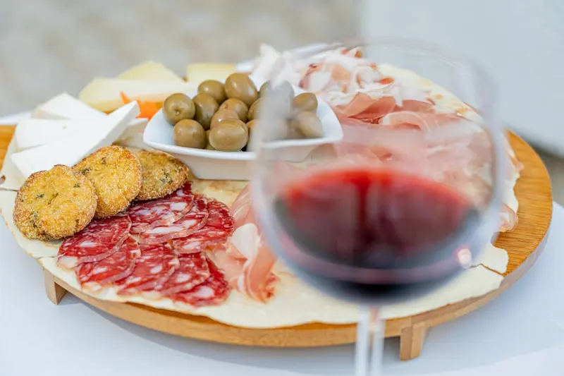 Assortiment de charcuterie, fromages et olives servis avec un verre de vin rouge.