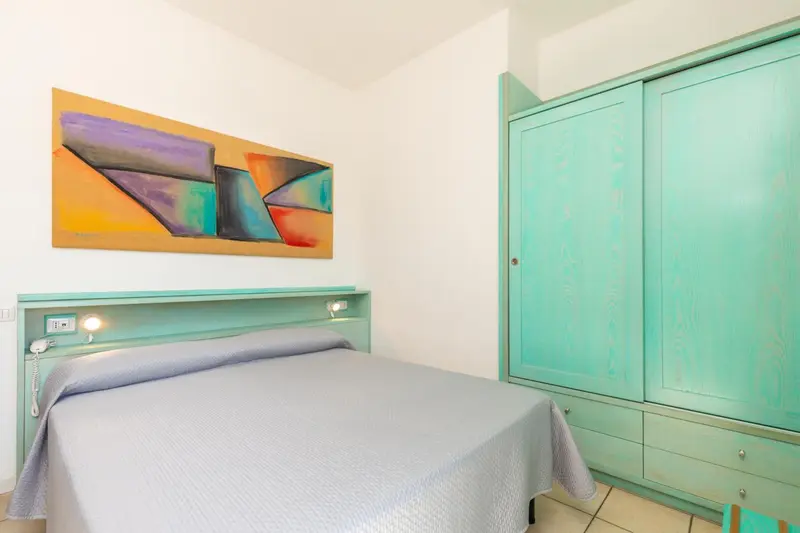 Une chambre lumineuse avec un lit et une armoire turquoise.