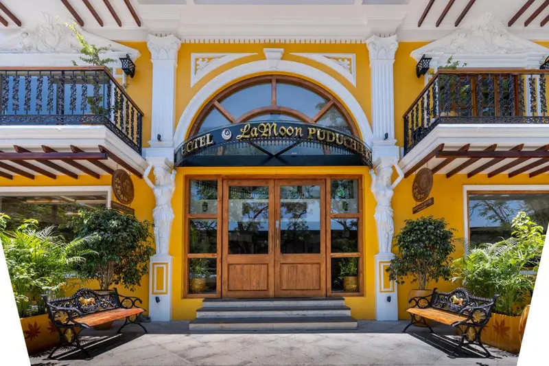 Facade jaune d'un bâtiment avec une entrée arquée et des balcons en fer forgé.