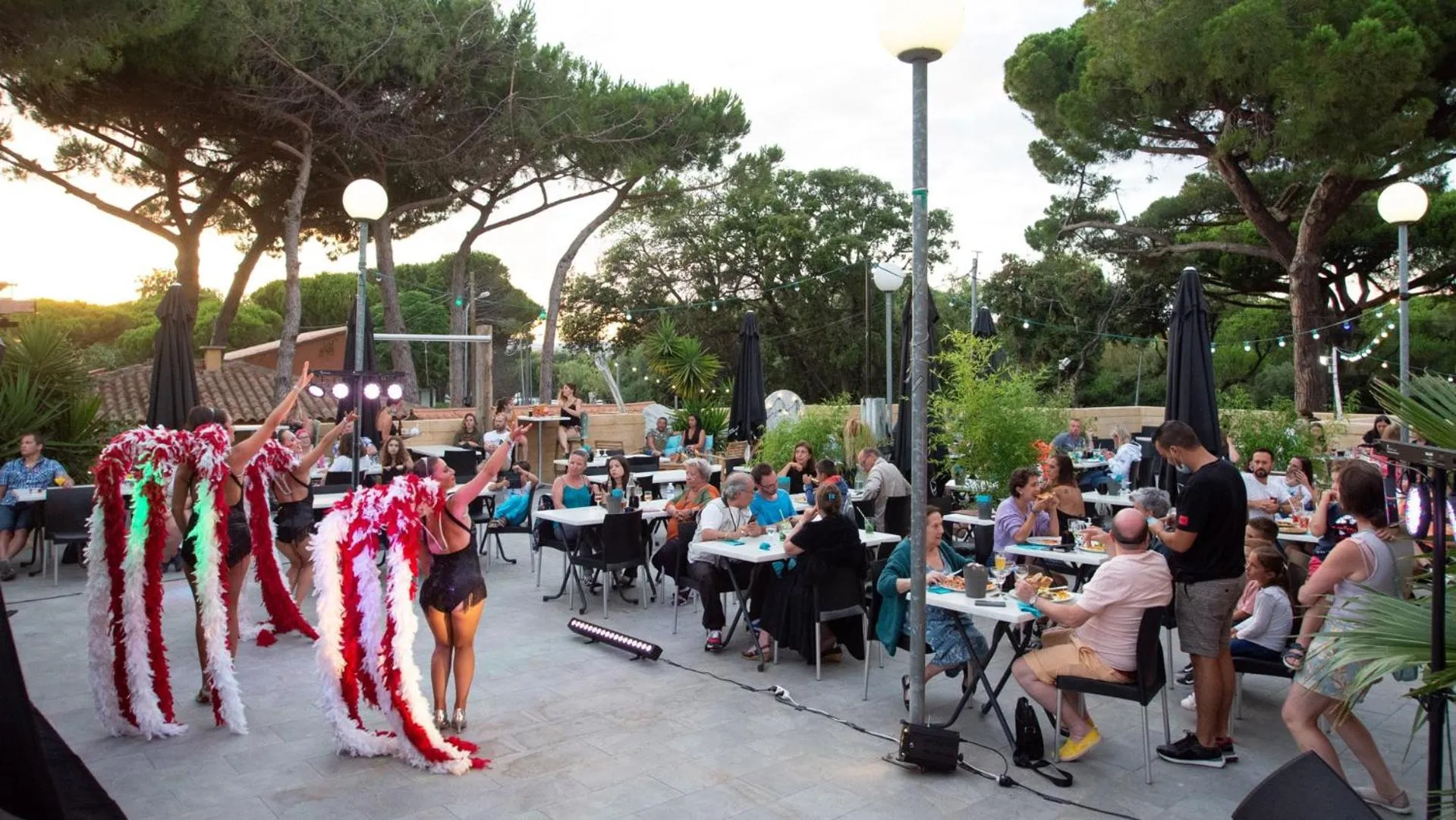 Une scène festive se déroule sur une terrasse avec des danseurs et des convives attablés.
