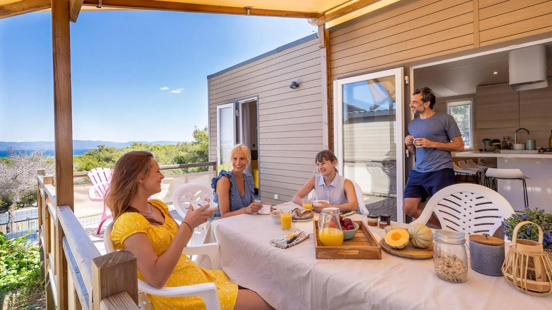 Une famille prend son petit-déjeuner sur une terrasse ensoleillée avec vue sur la mer.