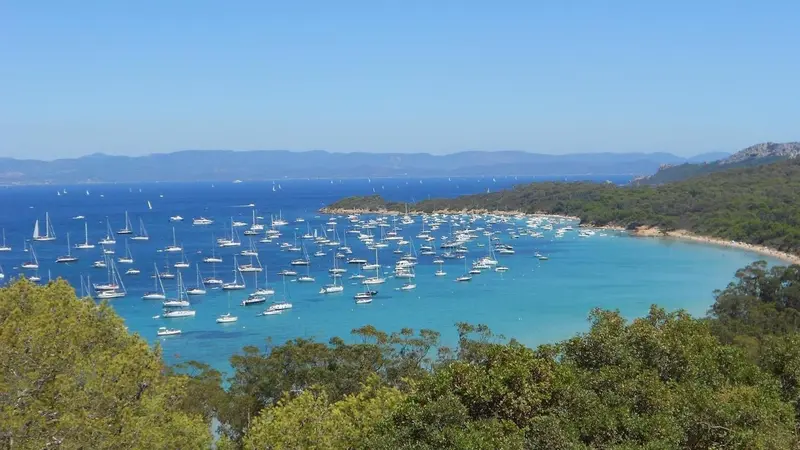 Vue aérienne d'une crique abritée avec de nombreux bateaux à voile amarrés dans une eau turquoise.