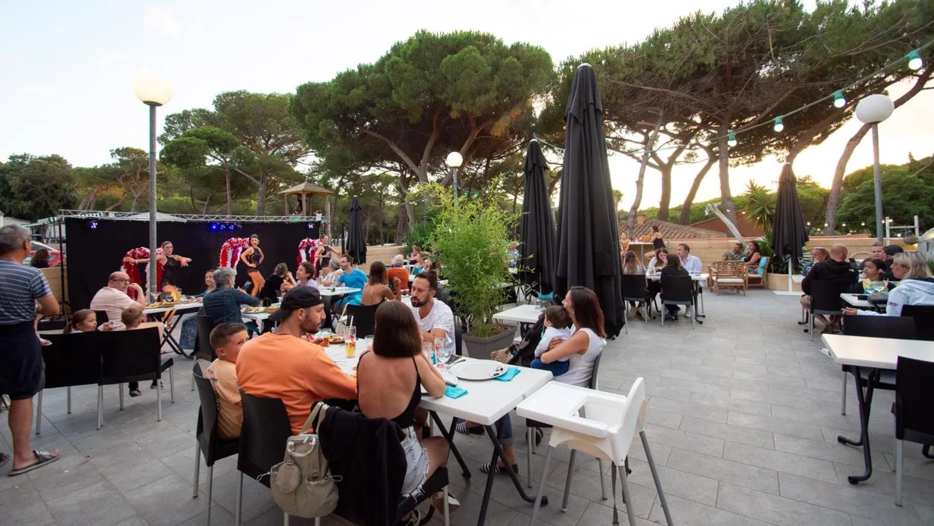 Une terrasse ombragée accueille des clients attablés et un spectacle en plein air.