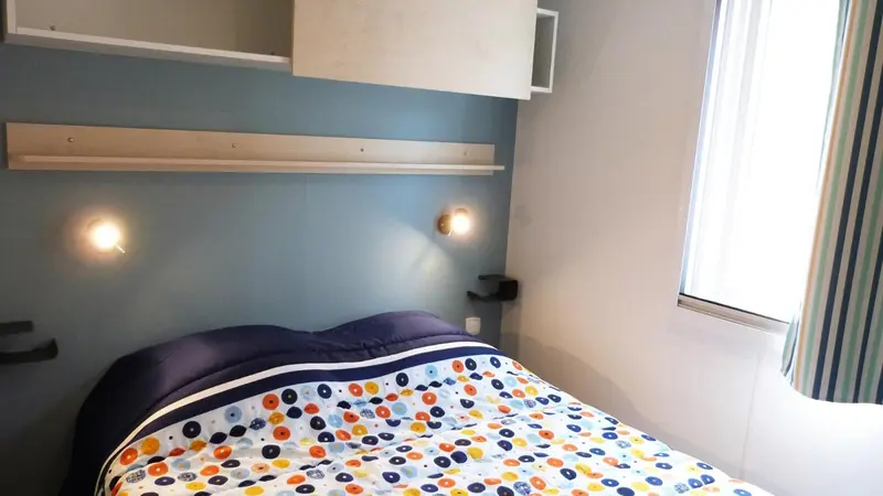 Un lit recouvert d'une couette colorée se trouve contre un mur bleu clair avec des lampes de chevet.