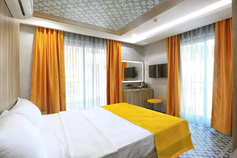 Chambre lumineuse avec un lit recouvert d'une courtepointe jaune et des rideaux orange.