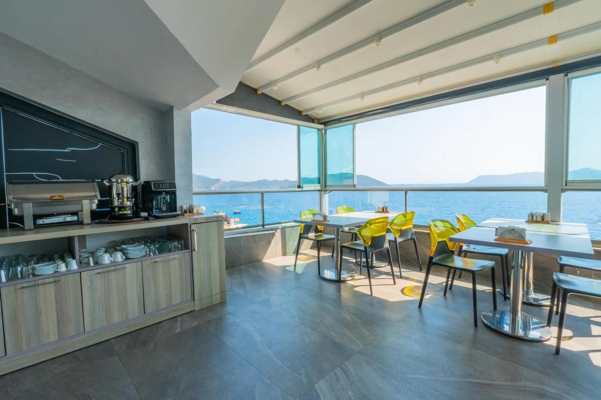 Une salle lumineuse avec un comptoir de buffet et des tables donnant sur la mer.