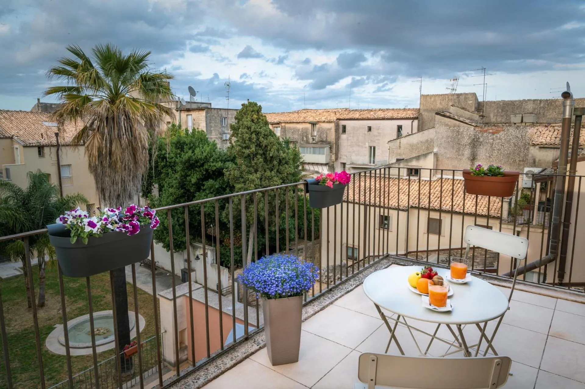 Une terrasse fleurie avec une table et des boissons fraîches offre une vue sur la ville.
