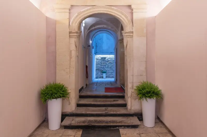 Un couloir voûté mène à une cour intérieure avec des plantes en pot.