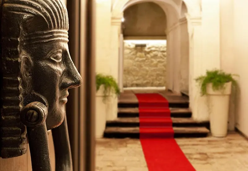 Un couloir d'hôtel est éclairé par un tapis rouge et décoré d'une statue égyptienne.