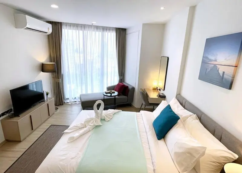 Une chambre lumineuse avec un lit fait et un coin salon près d'une fenêtre.