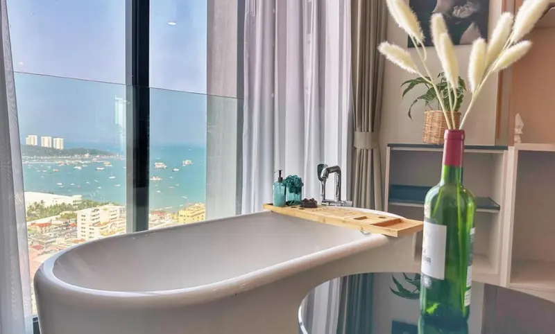 Une baignoire est placée devant une grande fenêtre avec vue sur la mer et la ville.