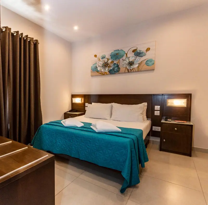 Une chambre avec un grand lit recouvert d'une couverture turquoise et décorée de fleurs.