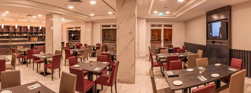 Une salle de restaurant lumineuse avec des tables dressées et un buffet en fond.