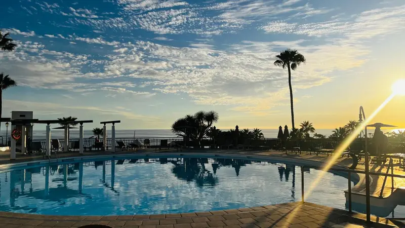 Une piscine turquoise reflète le ciel nuageux au coucher du soleil.