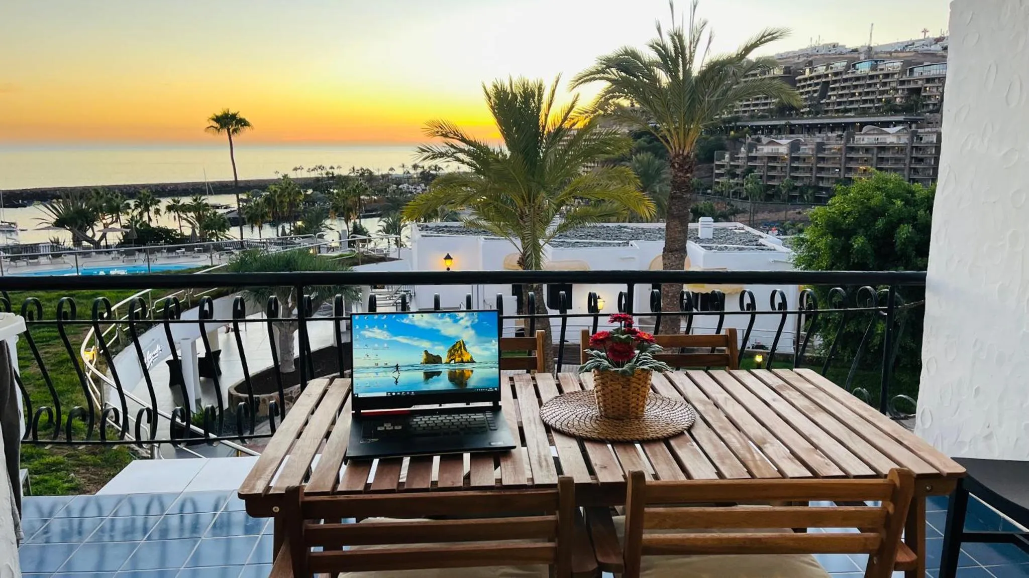 Une table et des chaises en bois sur une terrasse avec vue sur la mer et un coucher de soleil.
