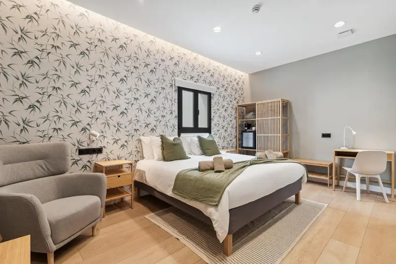 Une chambre lumineuse avec un lit fait et un coin salon.