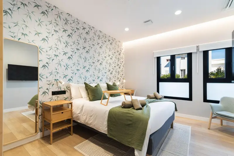 Une chambre lumineuse avec un grand lit et un décor mural végétal.
