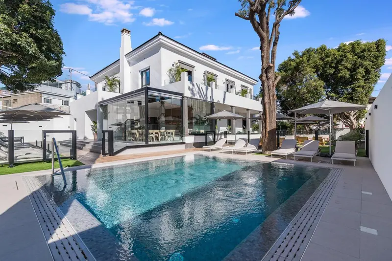 Une piscine rectangulaire turquoise bordée d'une terrasse avec des transats et des parasols.