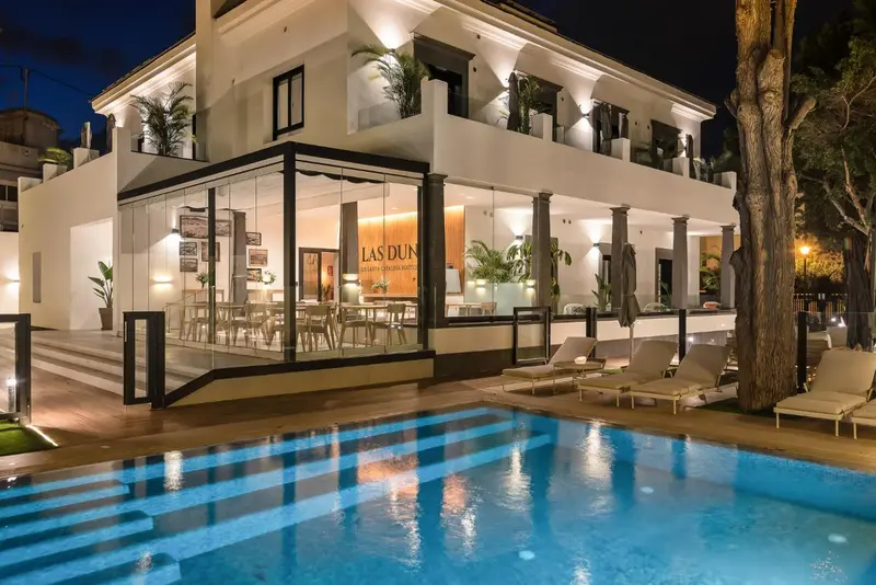 Façade blanche d'un bâtiment avec une piscine au premier plan et une terrasse éclairée.
