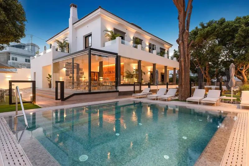 Bâtiment blanc moderne avec piscine et chaises longues au premier plan.