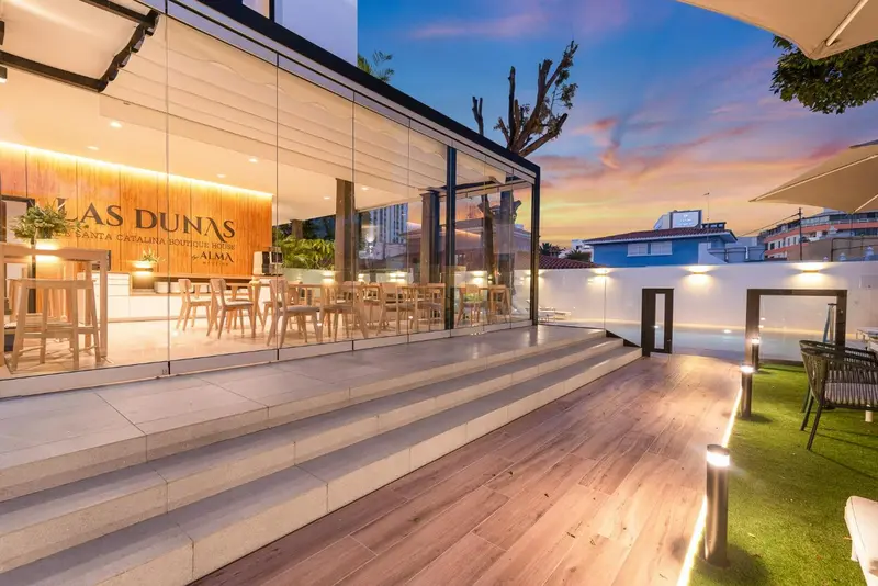 Terrasse en bois avec mobilier d'extérieur devant une façade vitrée illuminée.