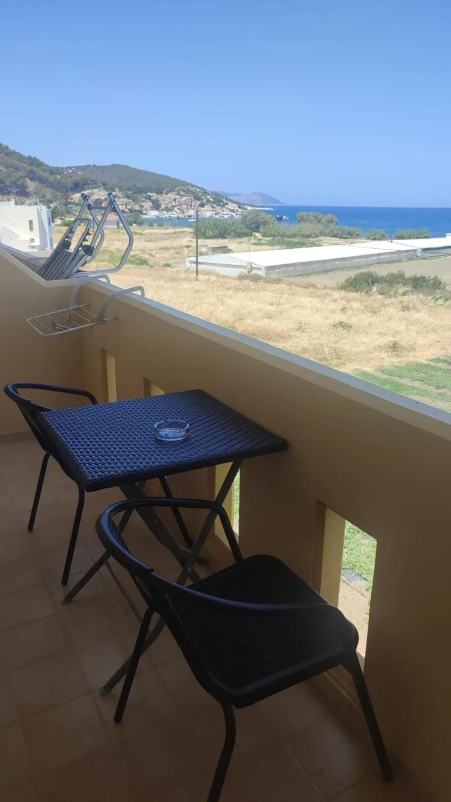 Une terrasse avec une table et des chaises offre une vue sur la mer et les collines.