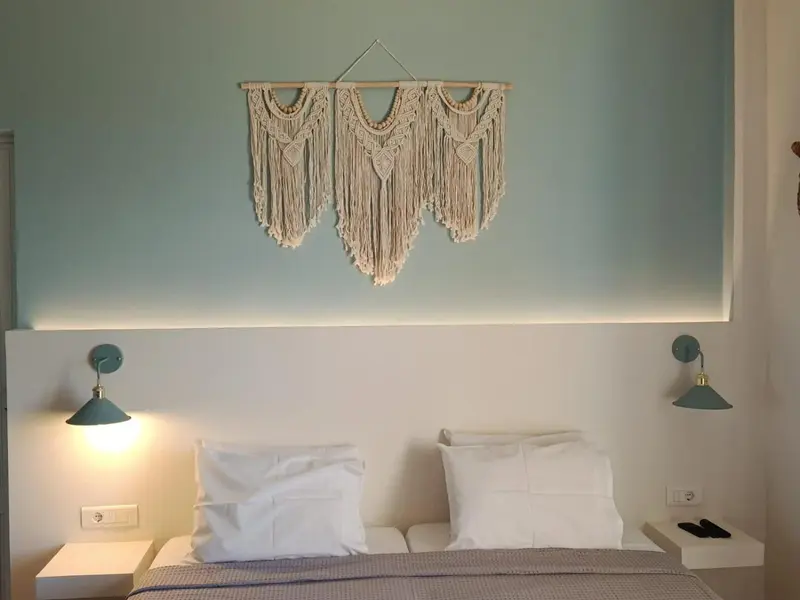 Une chambre lumineuse avec un lit double et une décoration murale en macramé.