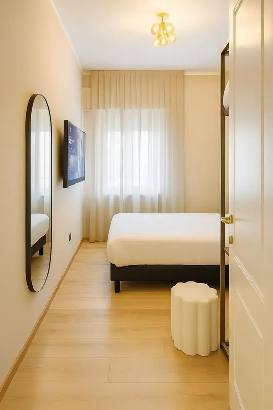 Chambre lumineuse avec un lit blanc et un miroir ovale.
