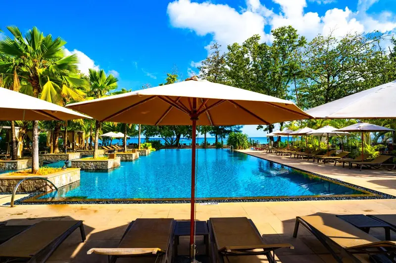 Transats et parasols bordent une piscine rectangulaire turquoise.