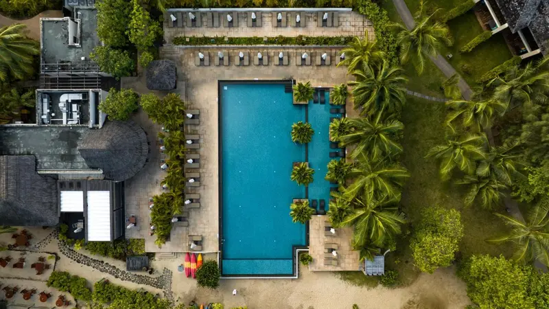 Vue aérienne d'une piscine rectangulaire entourée de chaises longues et de végétation tropicale.