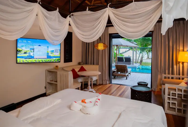 Une chambre lumineuse avec un lit décoré et une vue sur une piscine et un espace détente extérieur.