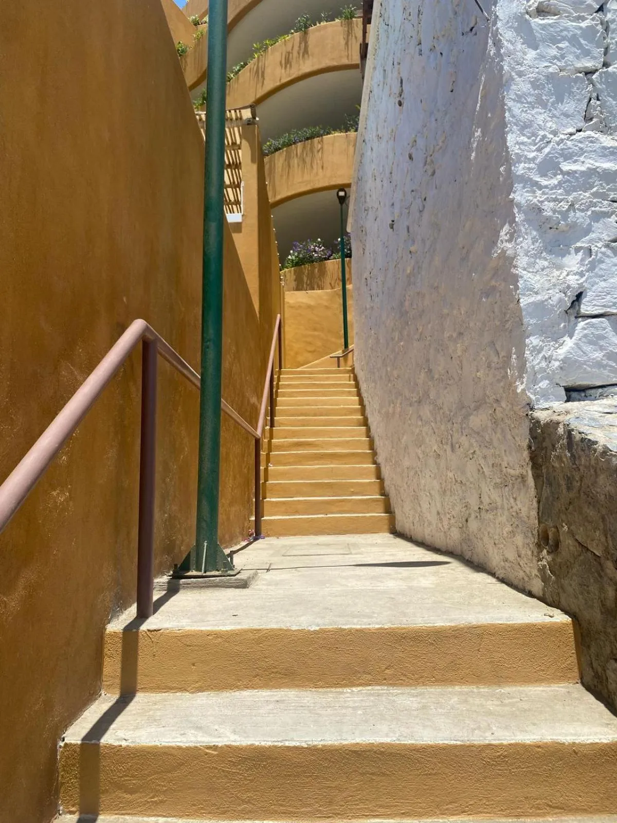 Un escalier jaune mène à une terrasse ombragée entre deux murs.