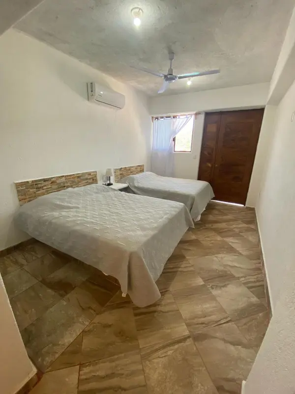 Une chambre lumineuse avec deux lits simples et un ventilateur au plafond.