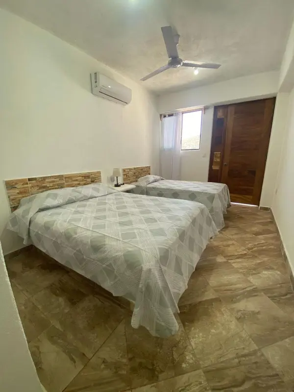Chambre lumineuse avec deux lits simples et un ventilateur au plafond.