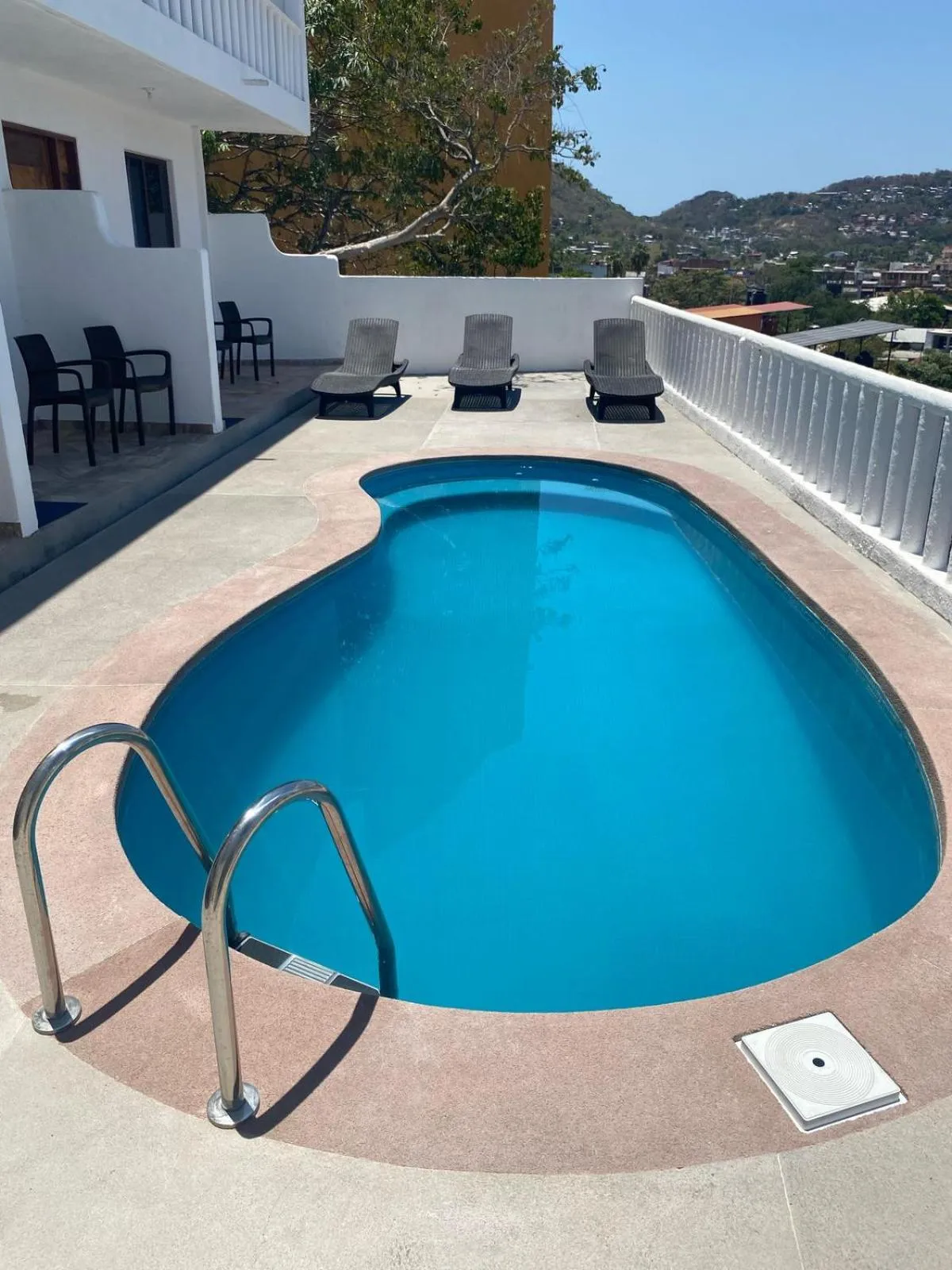 Une piscine rectangulaire avec des chaises longues sur une terrasse ensoleillée.