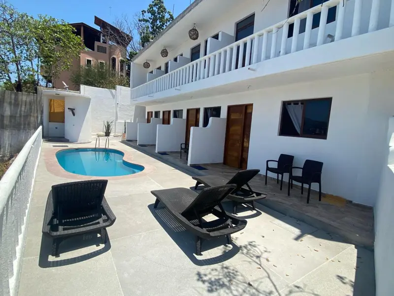 Transats noirs disposés autour d'une piscine rectangulaire devant un bâtiment blanc à balcons.
