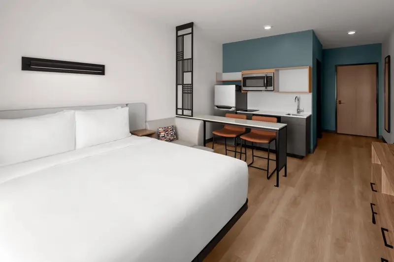 Une chambre lumineuse avec un lit blanc et un coin cuisine.