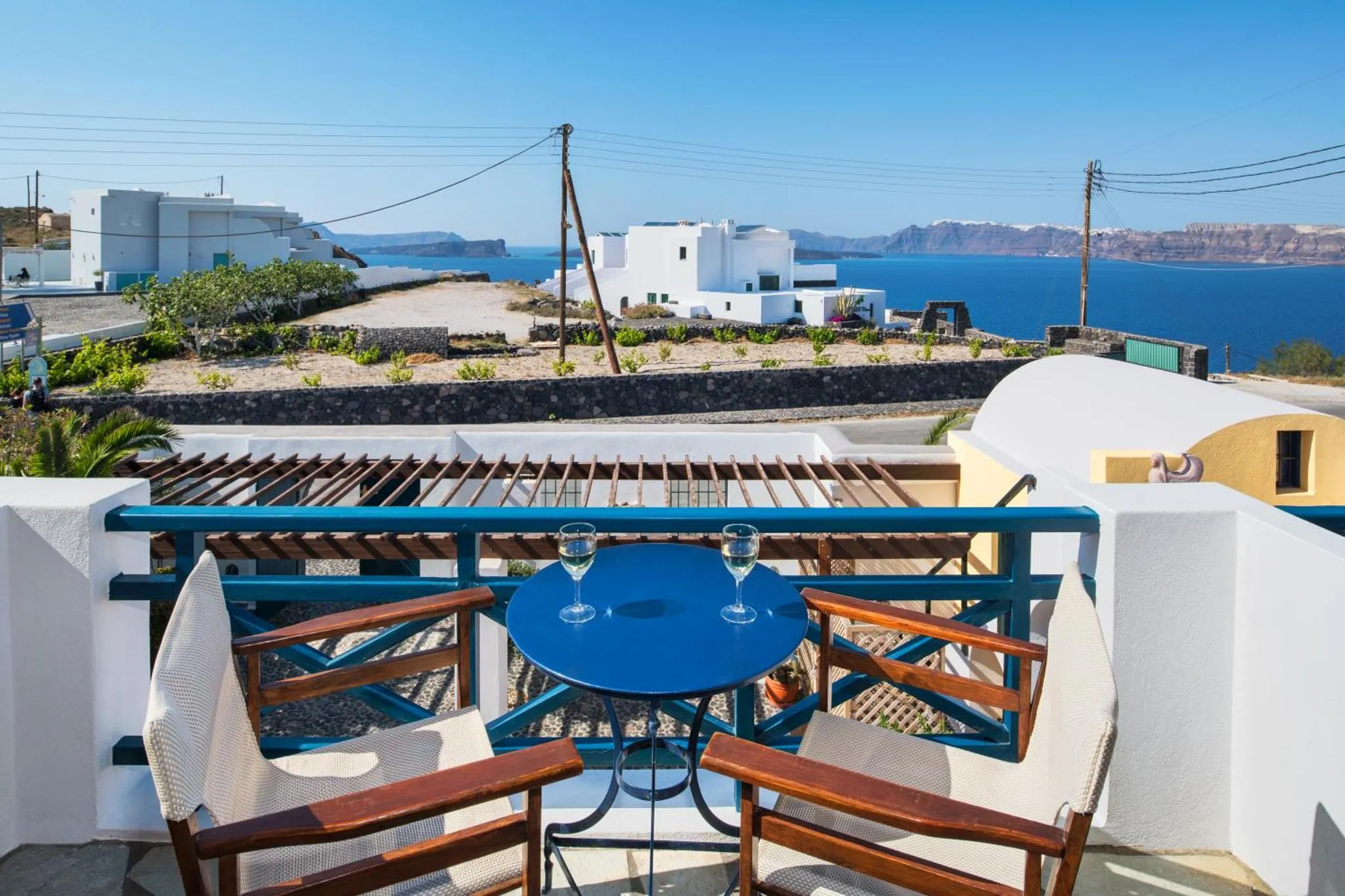Une table bleue avec deux verres à vin est posée sur une terrasse ensoleillée avec vue sur la mer.